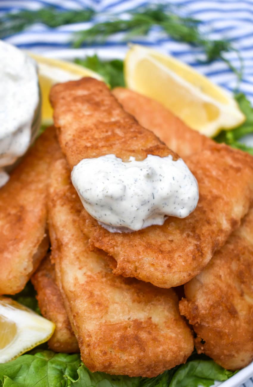 a pile of fried fish on a bed of lettuce on a white plate topped with a dollop of homemade tartar sauce