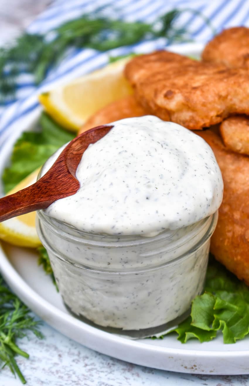 a wooden spoon scooping homemade tartar sauce out of a small glass jar