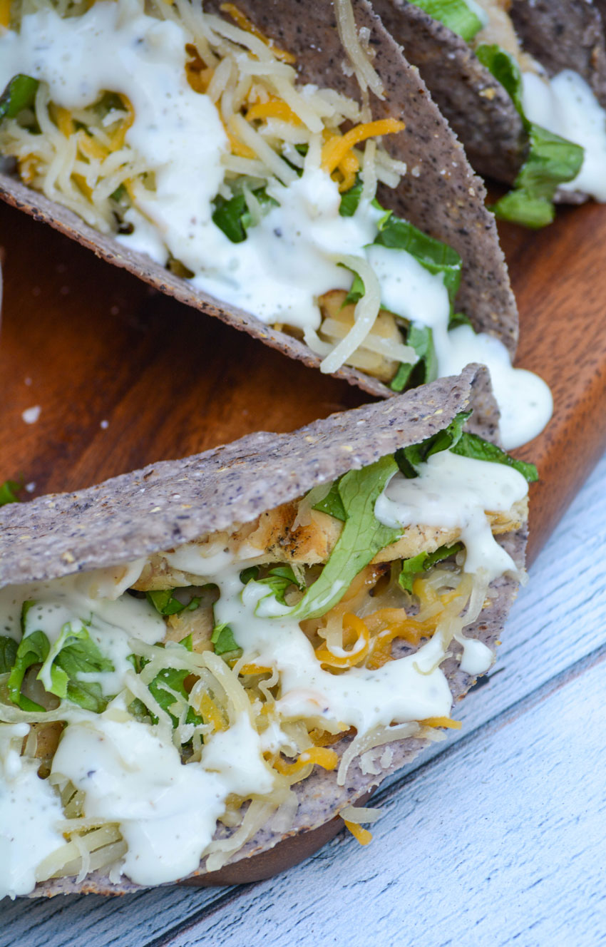 ranch chicken tacos drizzled with creamy ranch dressing and resting on a wooden cutting board