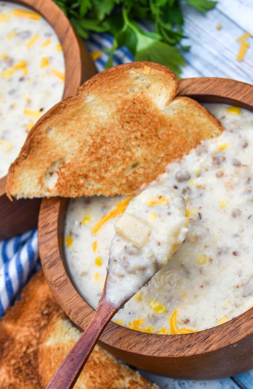 a small wooden spoon holding up a scoop of sausage and grits chowder