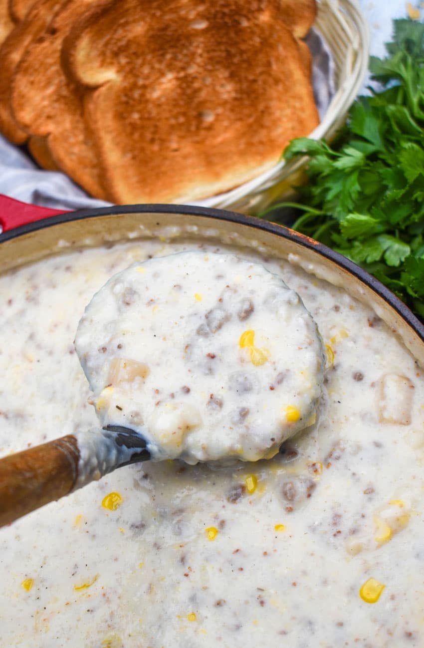 a wooden handled spatula scooping sausage and grits chowder out of a large dutch oven