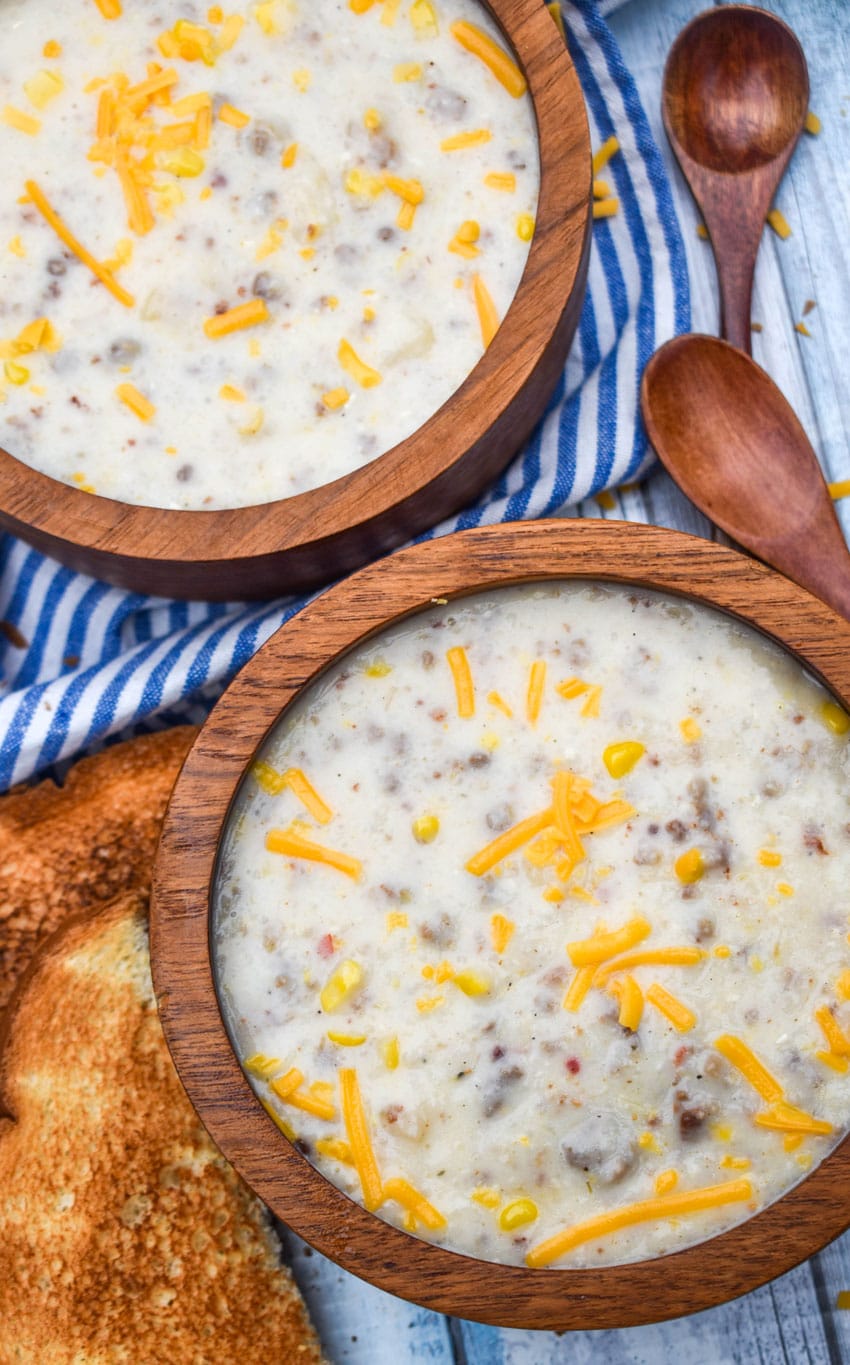 sausage and grits chowder in two wooden bowls with slices of toast on the side