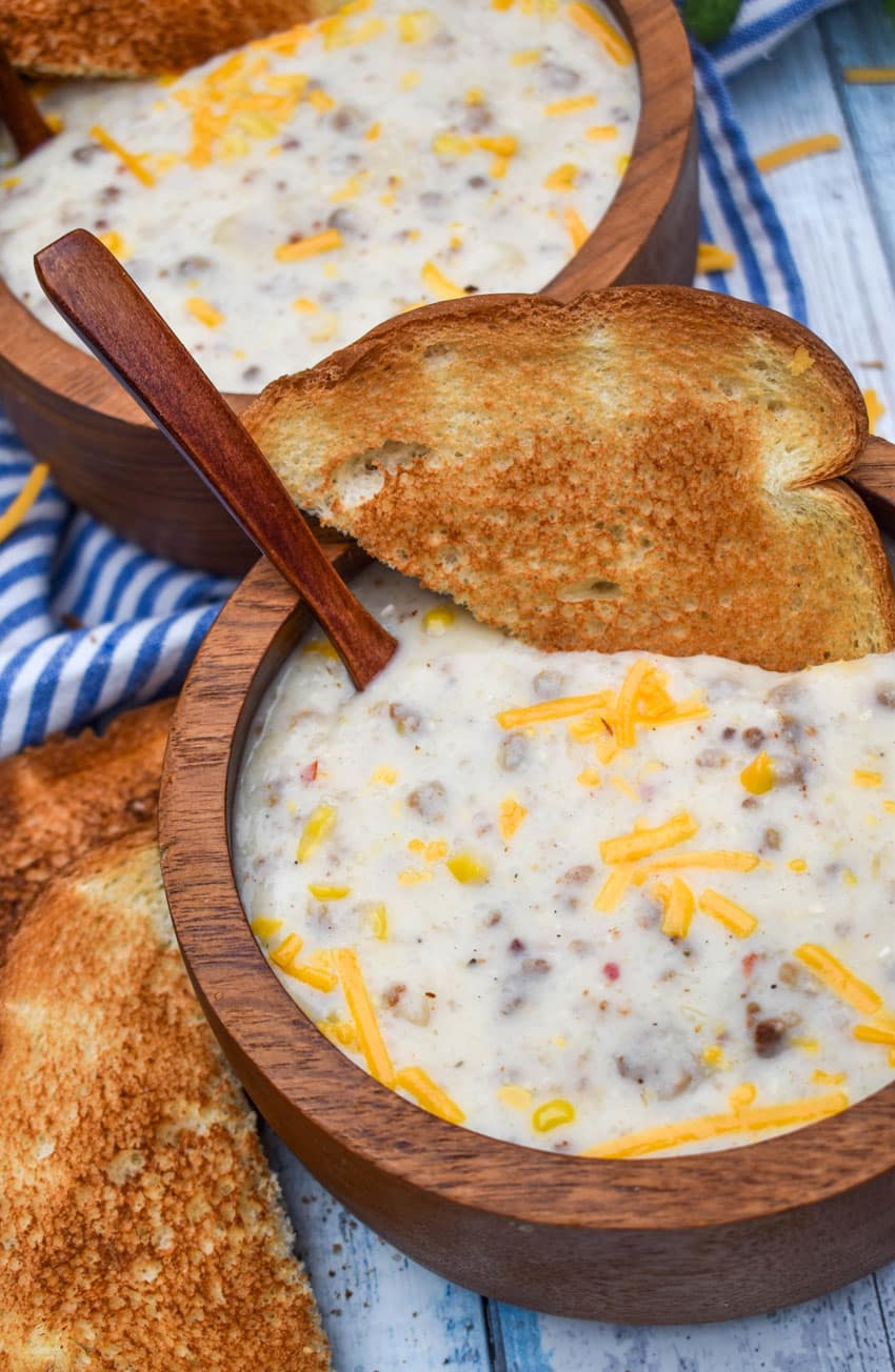 sausage and grits chowder in two wooden bowls with slices of toast on the side