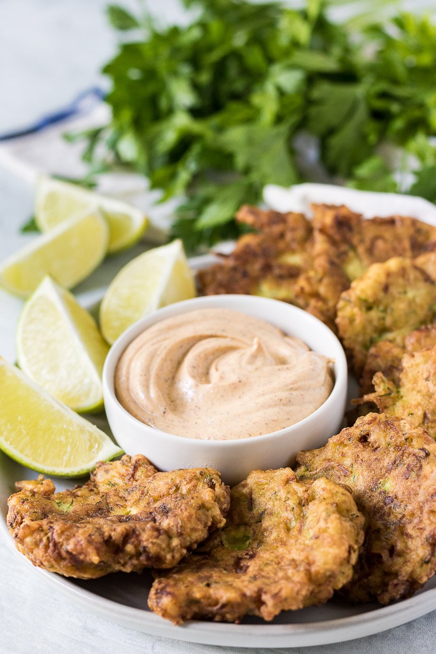 zucchini fritters arranged around a small bowl of dip on a white plate