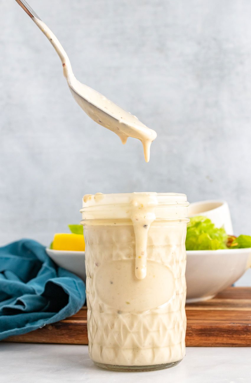 a spoon dripping homemade caesar dressing over a glass jar filled with dressing