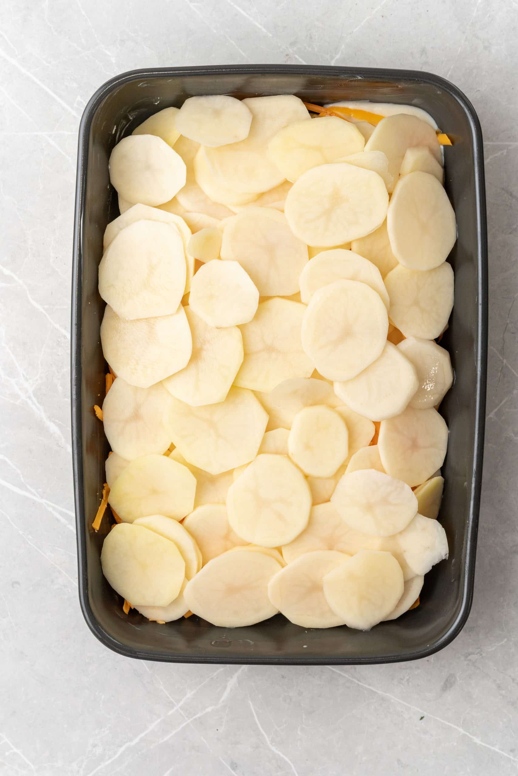 thinly sliced potatoes layered in a black casserole dish
