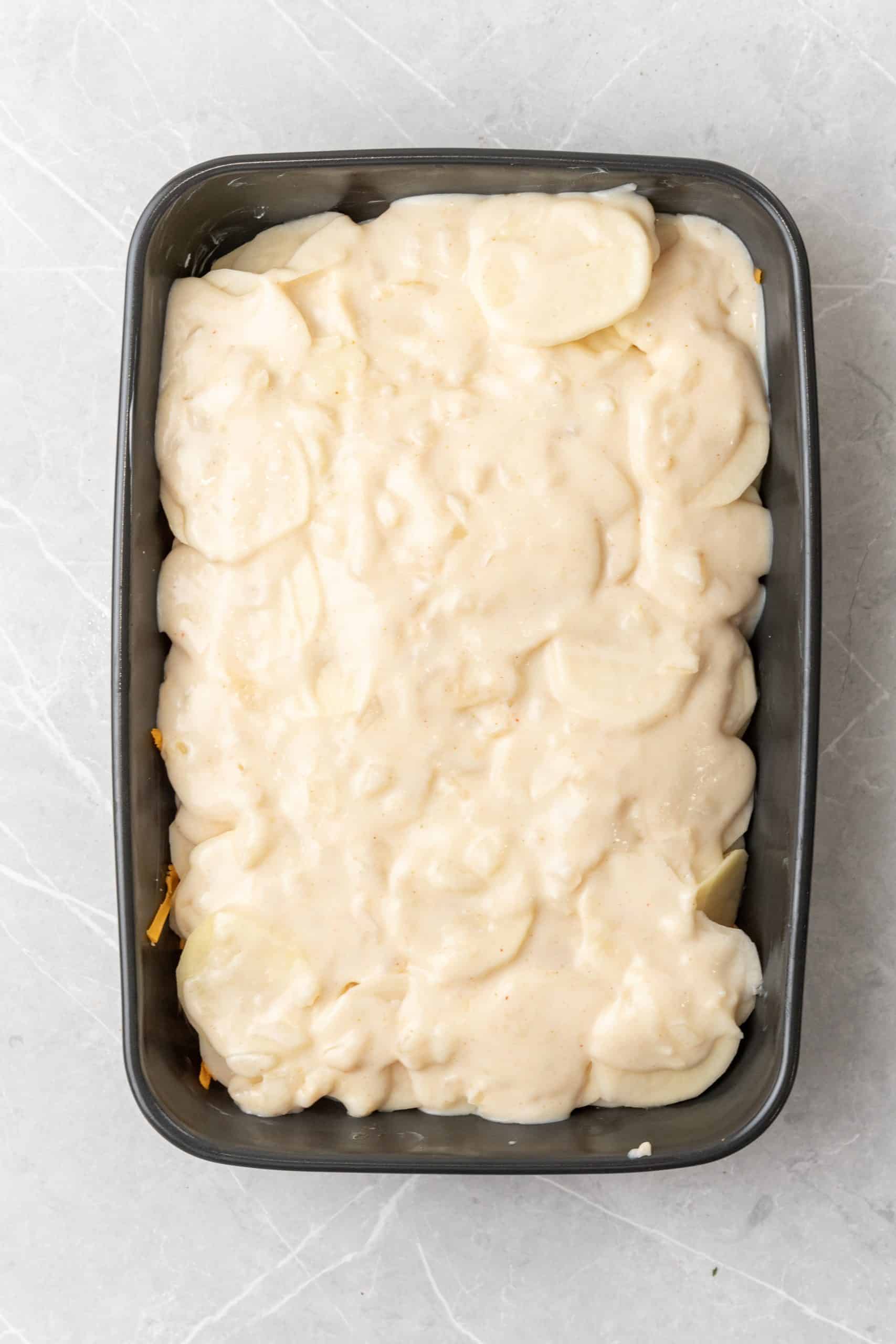 a creamy roux spread over thinly sliced potatoes in a black casserole dish