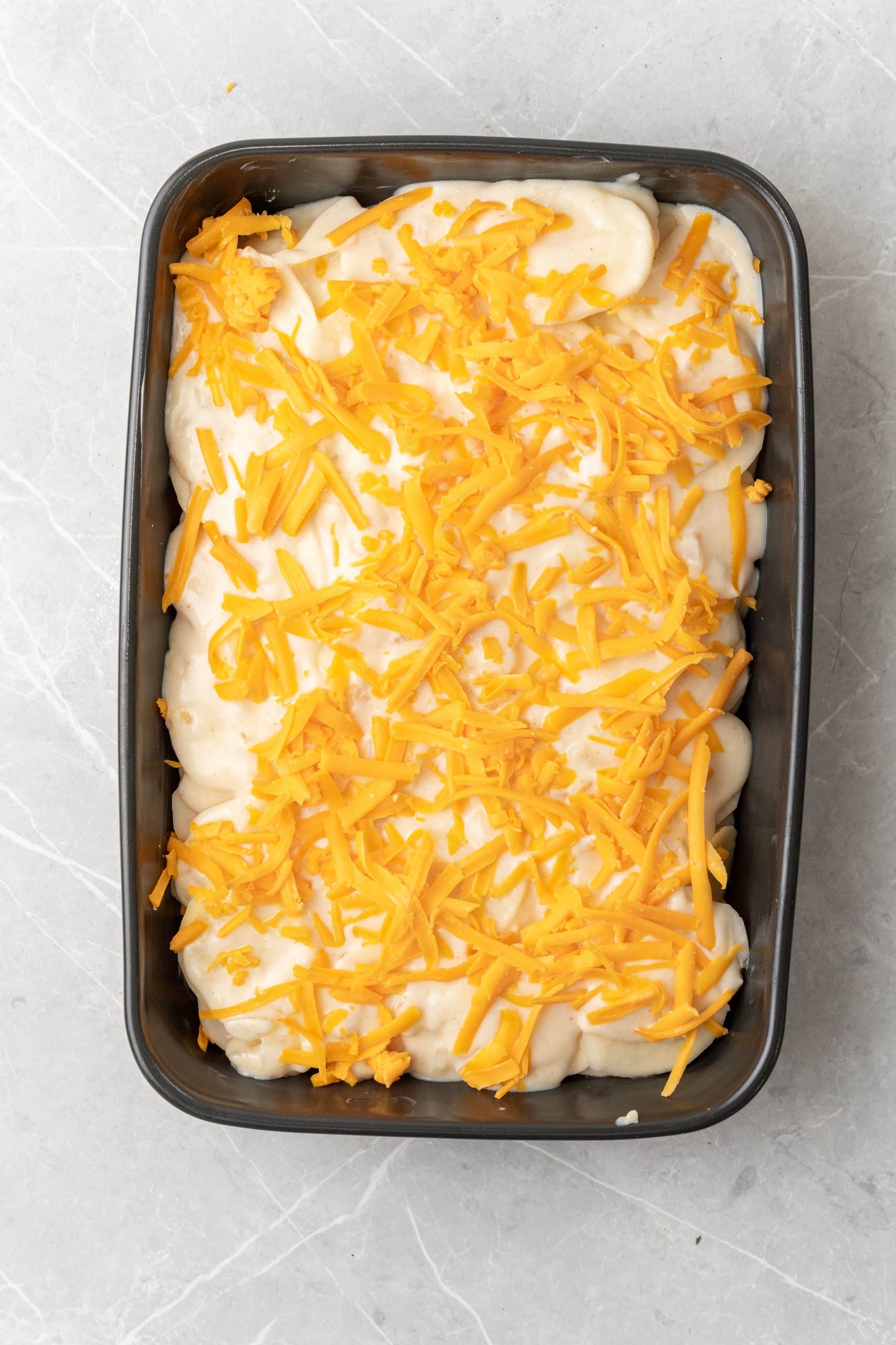 shredded cheddar cheese on top of a creamy potato casserole in a black baking dish