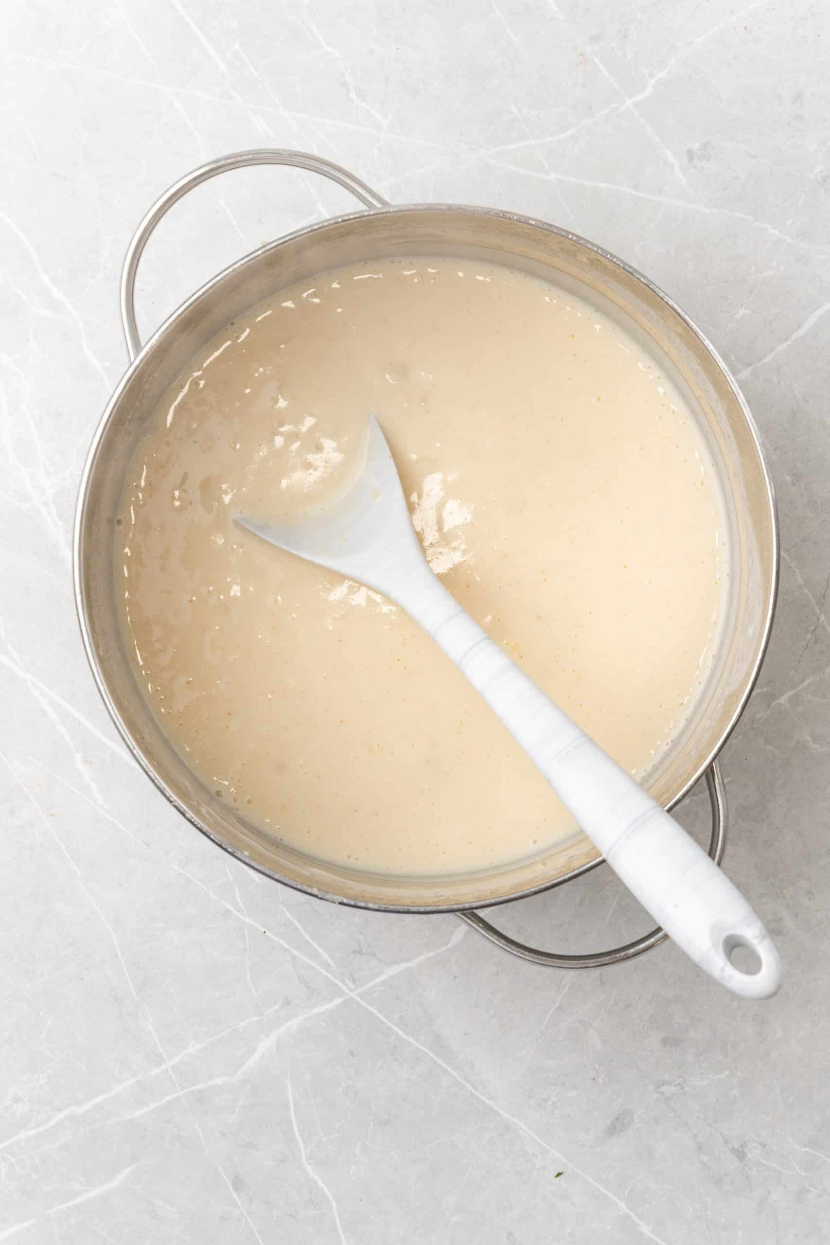 a white spoon stuck in a creamy roux in a silver pot