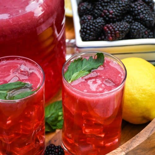 blackberry lemonade in two small glasses on a wooden serving tray