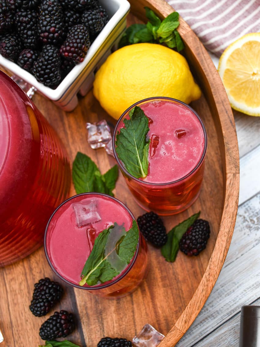 blackberry lemonade in two small glasses on a wooden serving tray