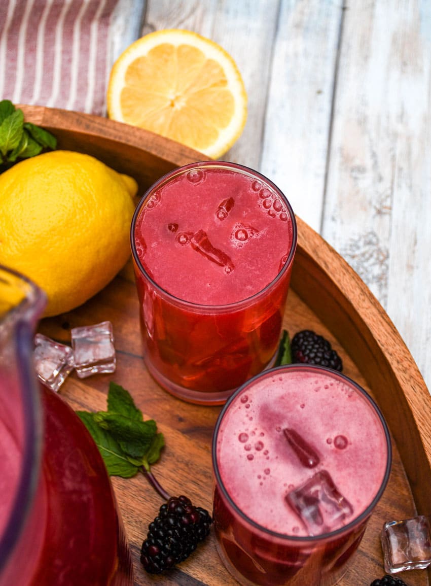 blackberry lemonade in two small glasses on a wooden serving tray