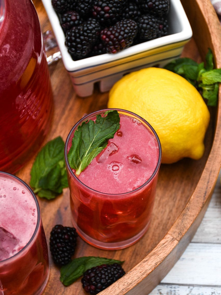 blackberry lemonade in two small glasses on a wooden serving tray