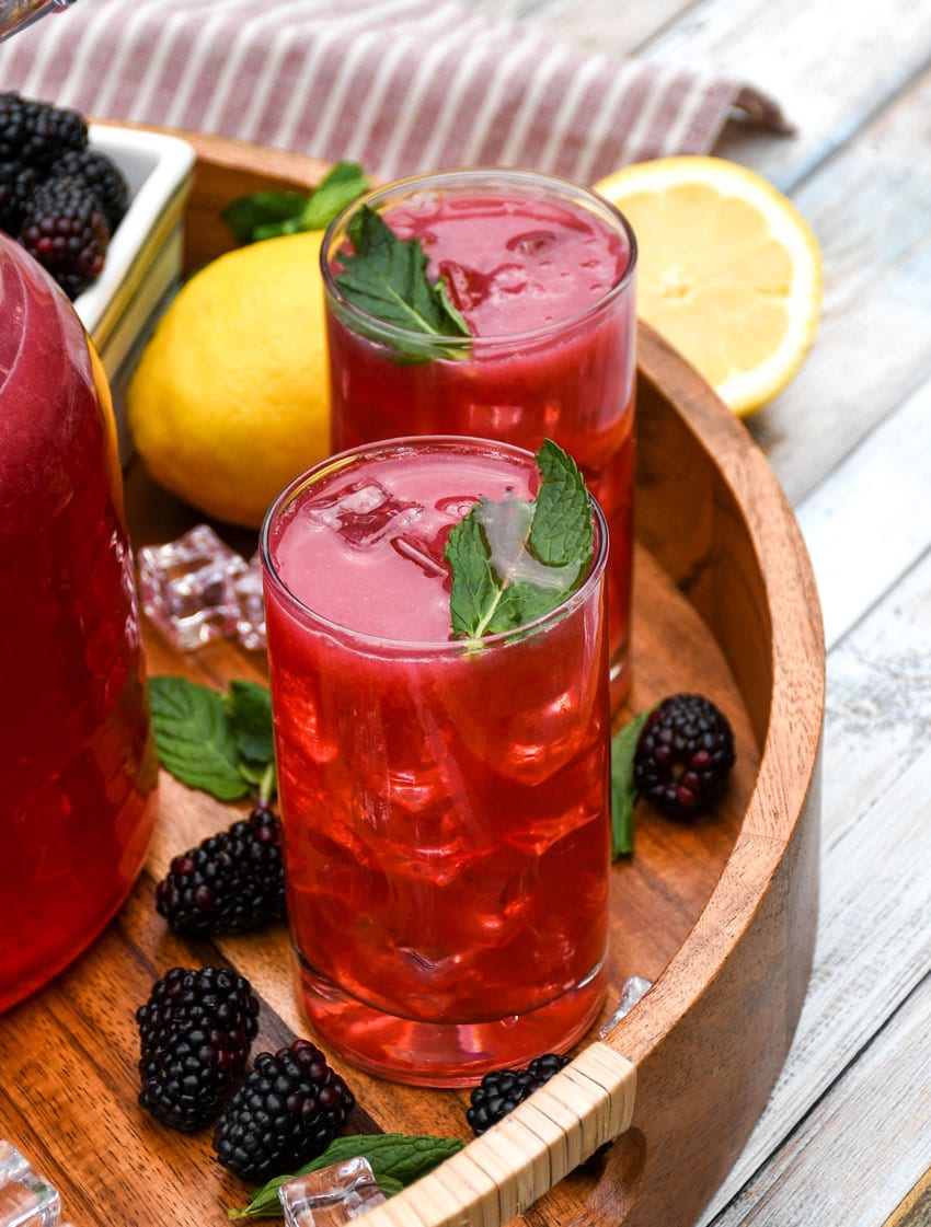 blackberry lemonade in two small glasses on a wooden serving tray