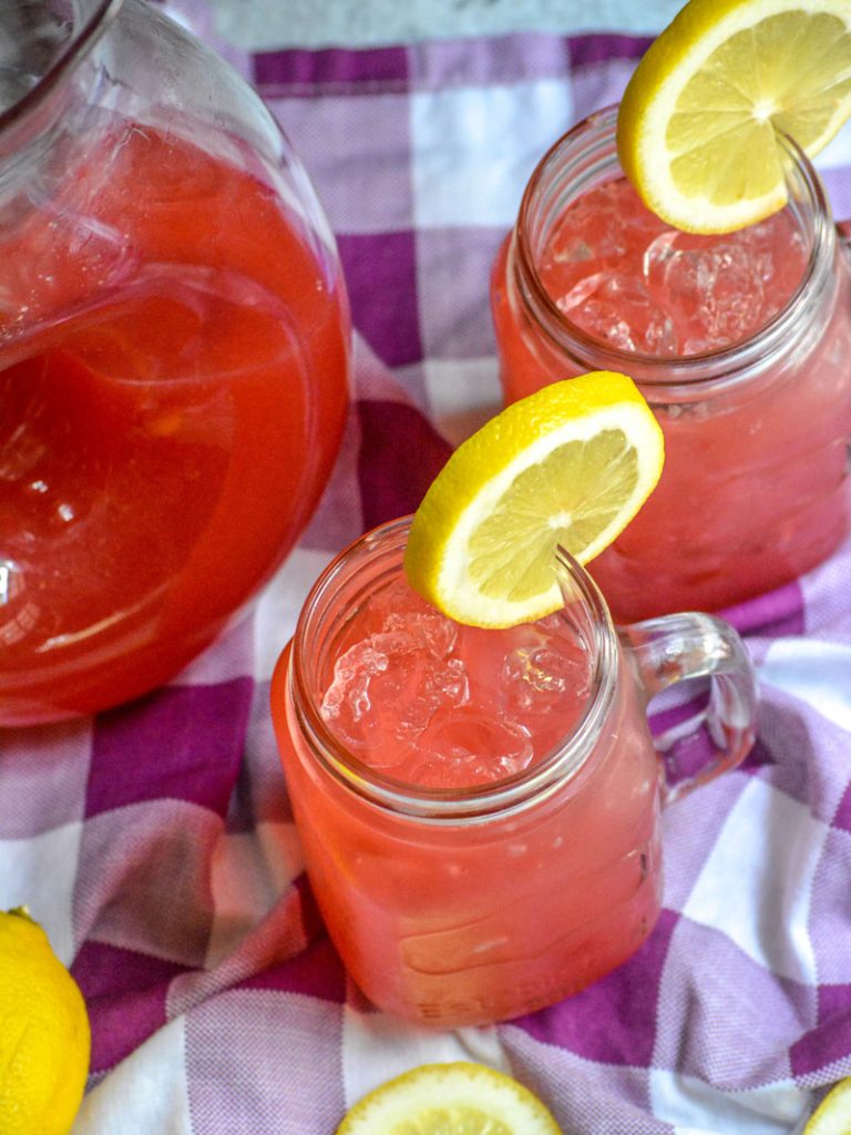 fresh blackberry lemonade served over ice in glass jars with a slice of lemon for garnish