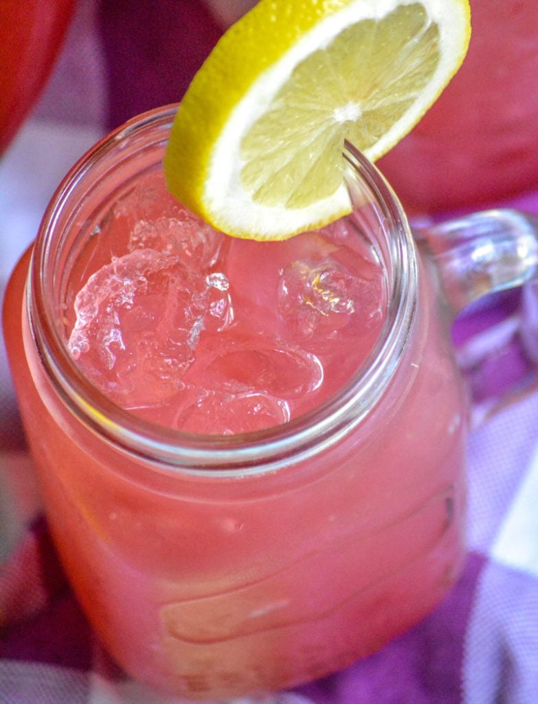 fresh blackberry lemonade served over ice in glass jars with a slice of lemon for garnish
