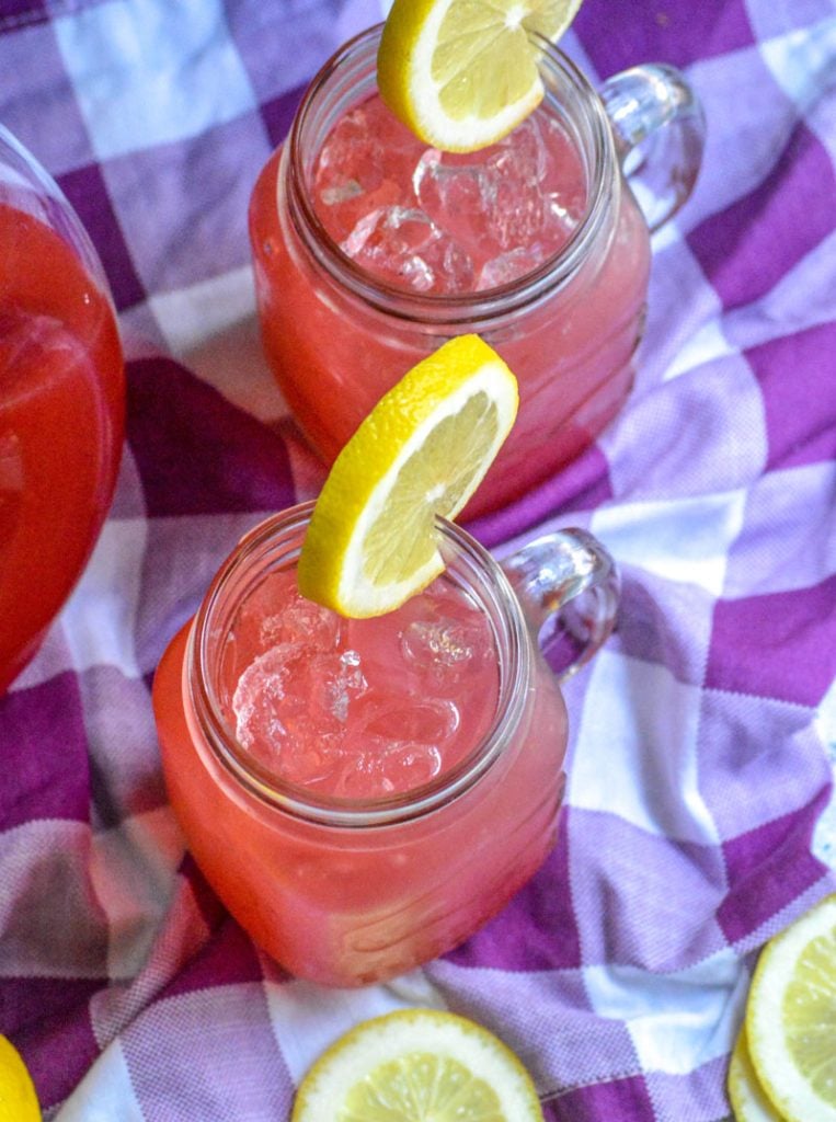 fresh blackberry lemonade served over ice in glass jars with a slice of lemon for garnish