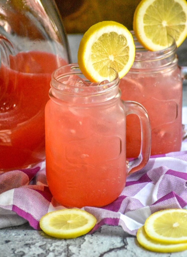 fresh blackberry lemonade served over ice in glass jars with a slice of lemon for garnish