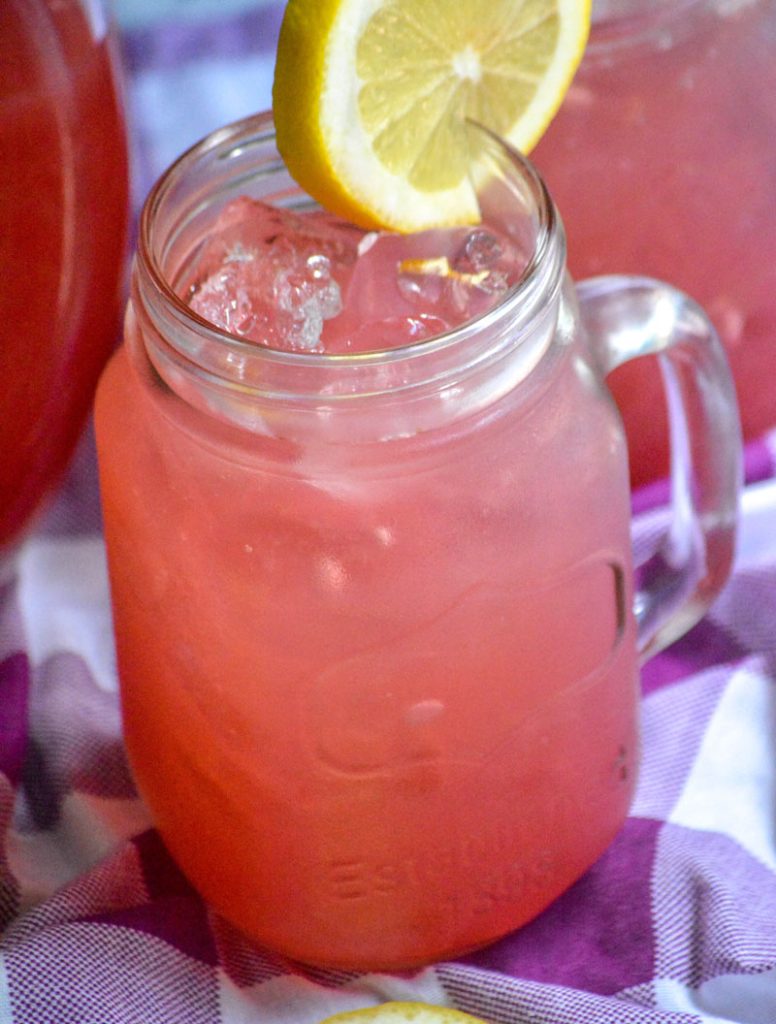 fresh blackberry lemonade served over ice in glass jars with a slice of lemon for garnish