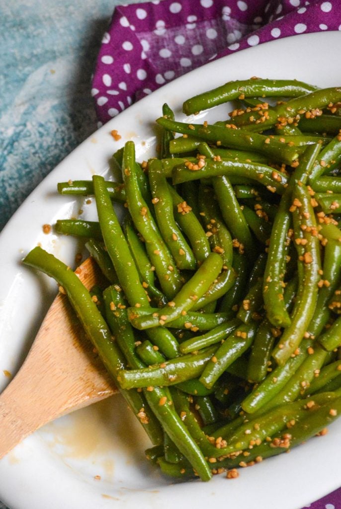 saucy garlic teriyaki green beans in a white serving dish with a wooden spoon