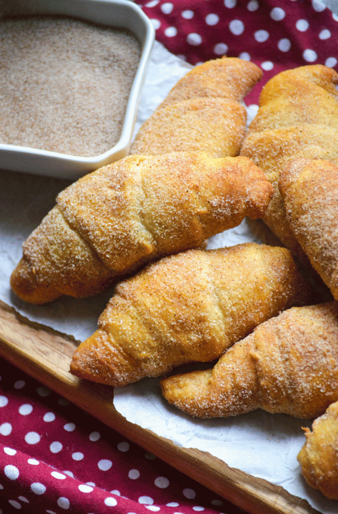 a pile of cinnamon sugar covered snickerdoodle crescent rolls on a wrinkled piece of white parchment paper