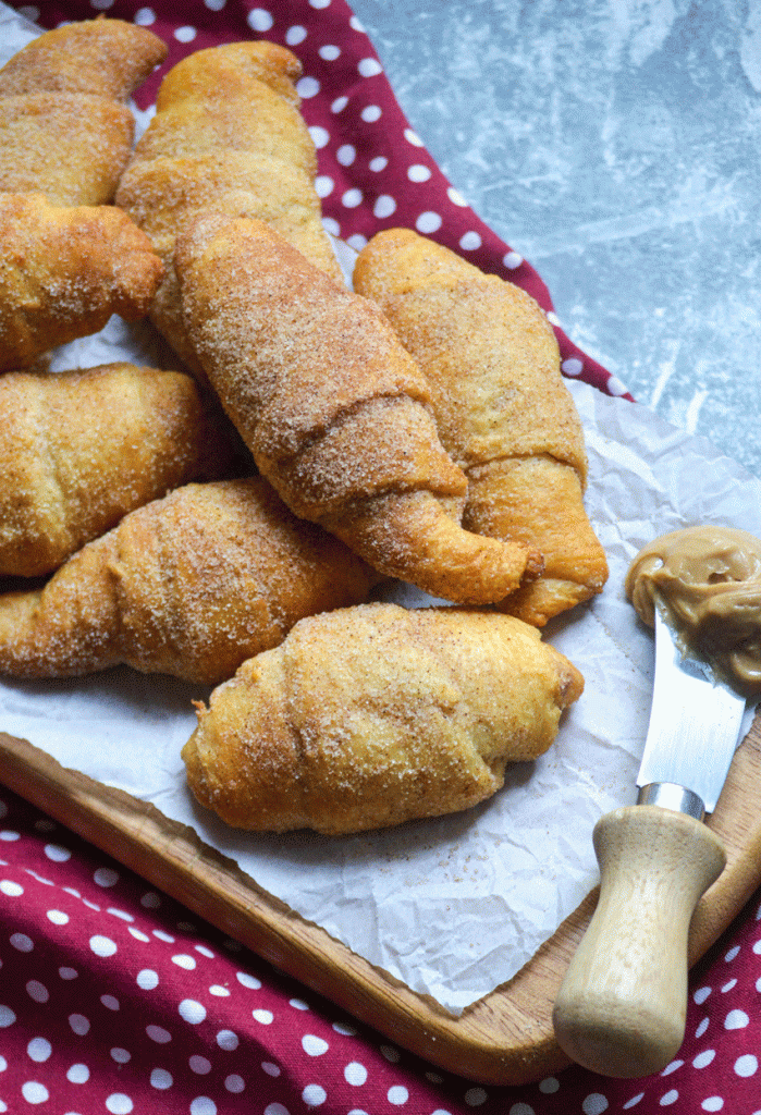 a pile of cinnamon sugar covered snickerdoodle crescent rolls on a wrinkled piece of white parchment paper