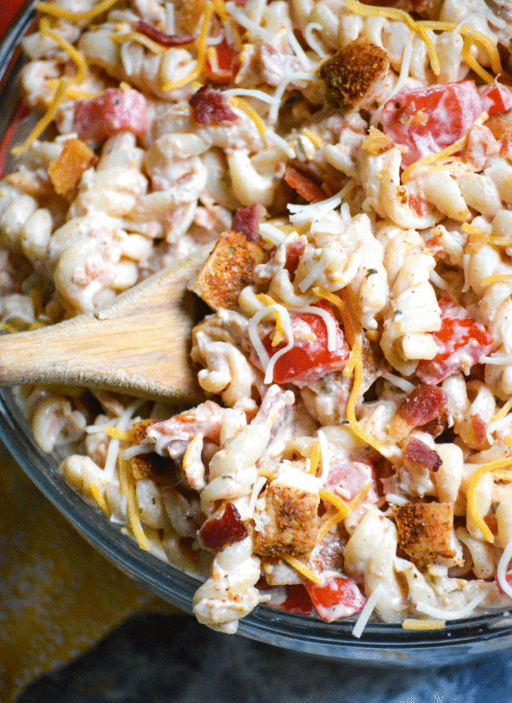 a wooden spoon scooping up a serving of Southwestern chicken pasta salad from a glass mixing bowl