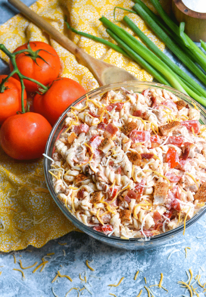 Southwestern chicken pasta salad served in a large glass mixing bowl with tomatoes and green onions in the background