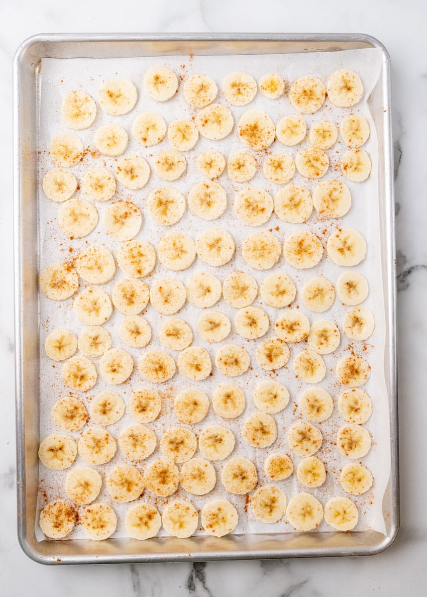 cinnamon sprinkled banana slices on a parchment paper lined baking sheet
