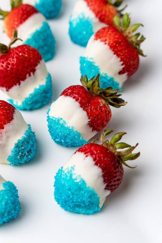 red white and blue chocolate dipped strawberries on a parchment covered baking sheet