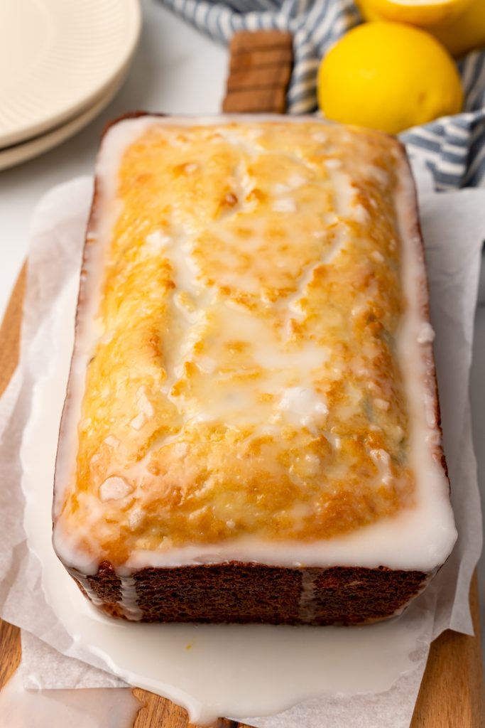 a glazed loaf of lemon zucchini bread on a parchment covered wooden cutting board