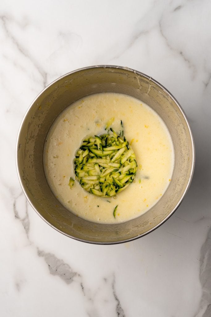 grated zucchini in a mixing bowl filled with yellow batter
