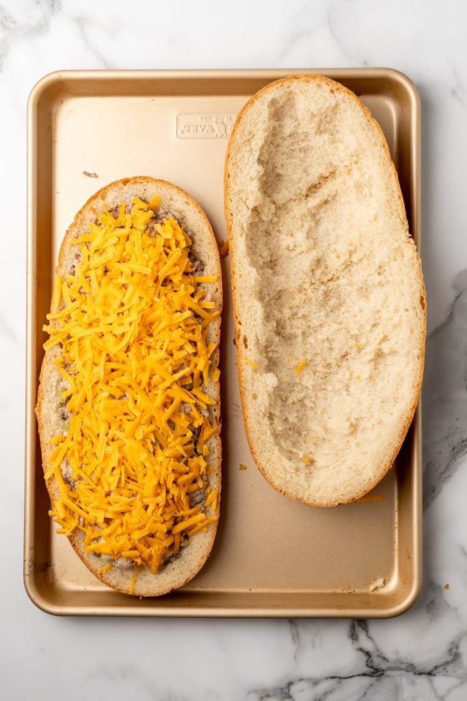 creamy ground beef mixture in a hollowed out loaf of french bread topped with shredded cheese on a metal baking sheet