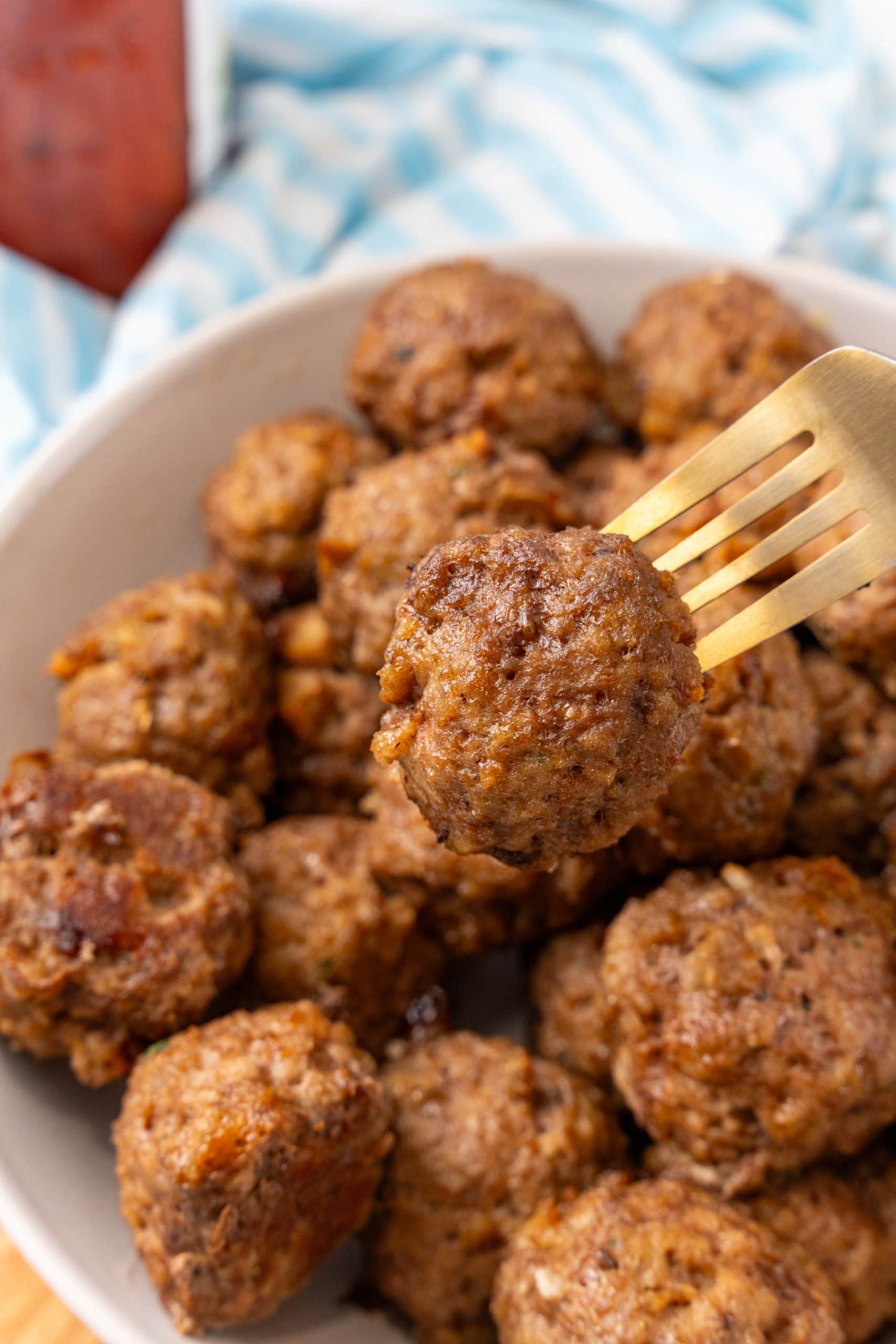 a golden fork holding up an easy baked meatball