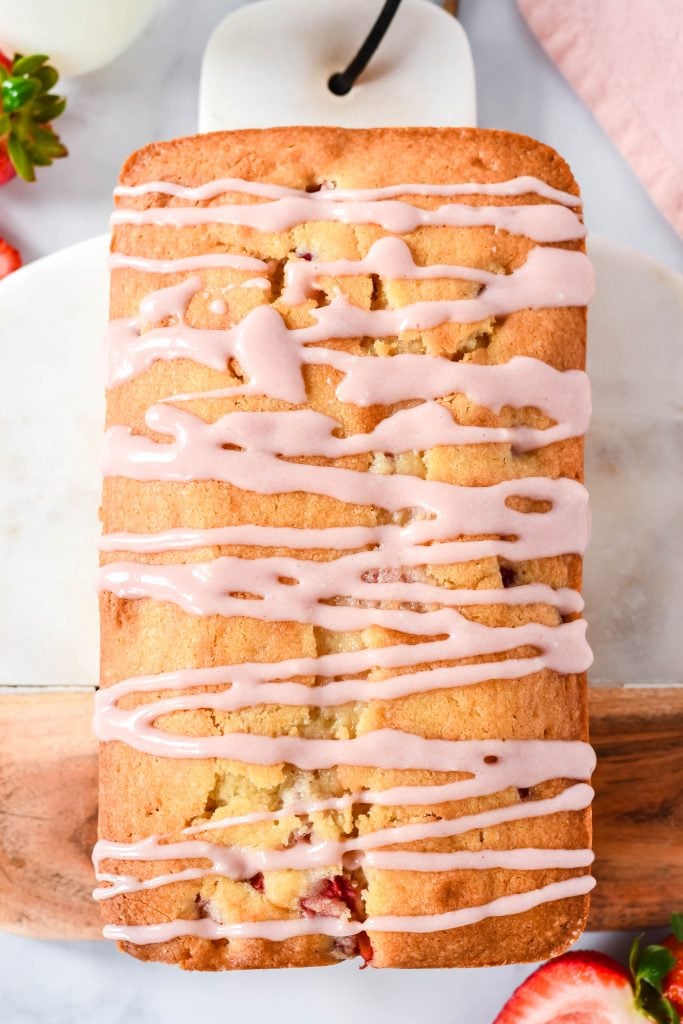 cream cheese glazed strawberry bread shown on a cutting board on a marble counter top