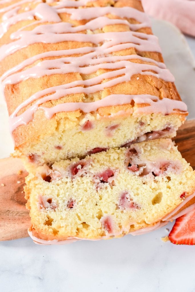 strawberry bread with cream cheese glaze served on a wooden cutting board on a marbled background