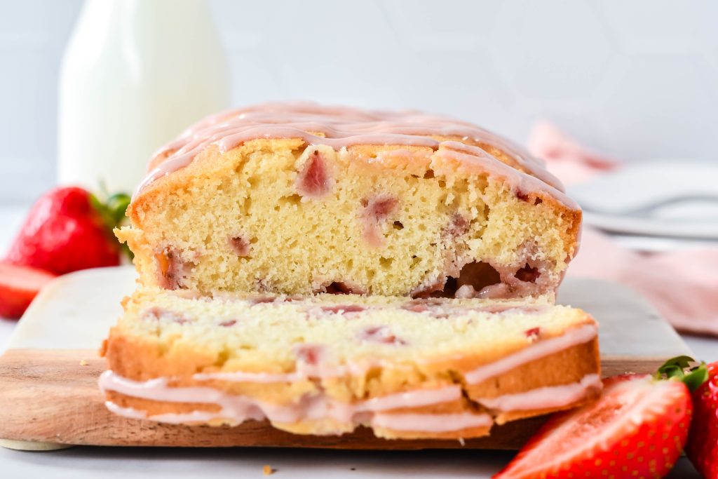 glazed strawberry bread shown sliced on a cutting board with fresh berries and a glass of milk