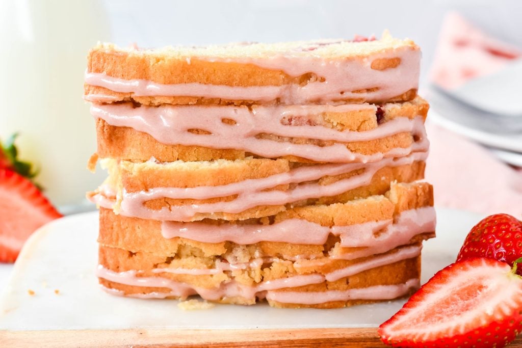 strawberry bread with a cream cheese glaze drizzle, shown sliced and stacked on a cutting board