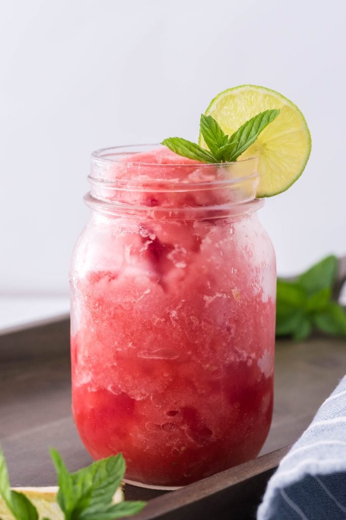 watermelon slush in a glass jar with a slice of lime and mint leaves on the rim for garnish