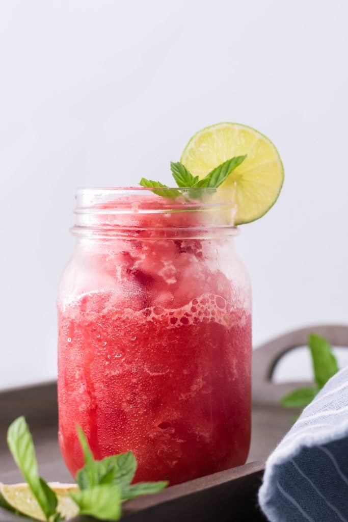 watermelon slushie in a glass jar with a slice of lime and mint leaves on the rim for garnish