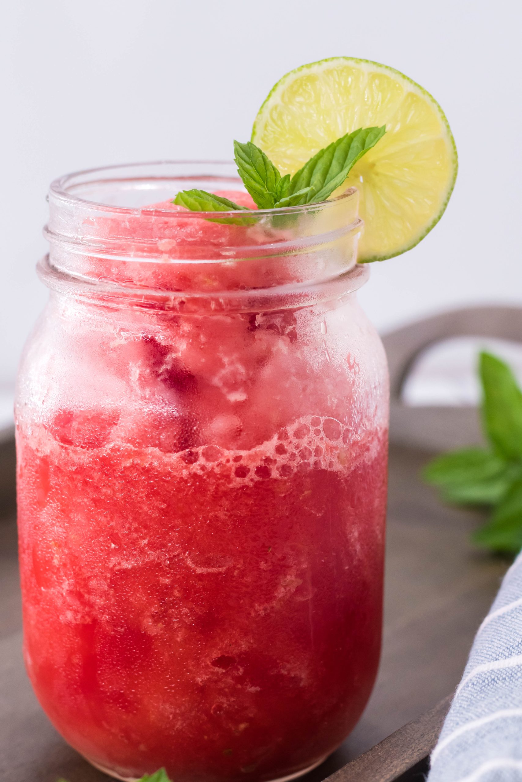 watermelon slushie in a glass jar with a slice of lime and mint leaves on the rim for garnish