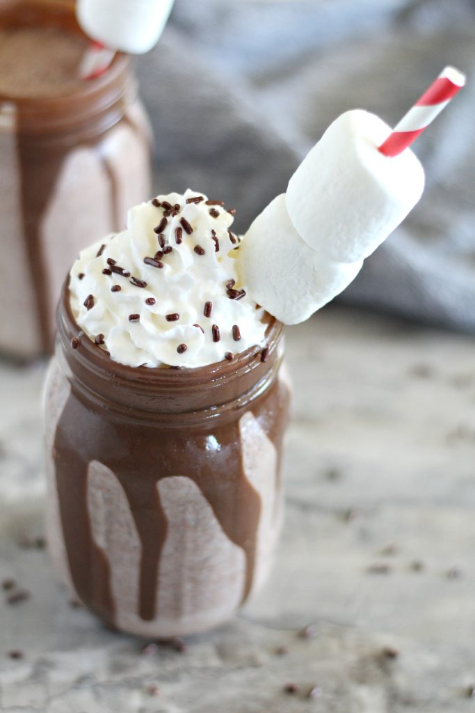 frozen hot chocolate in a mason jar topped with whipped cream, chocolate sprinkles, and a marshmallow laden straw