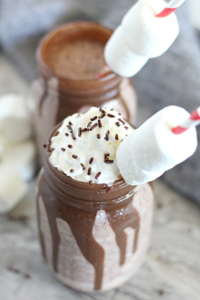 frozen hot chocolate in a mason jar topped with whipped cream, chocolate sprinkles, and a marshmallow laden straw