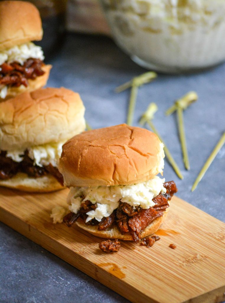 pulled pork slider sandwiches shown on a narrow wooden cutting board on a gray background