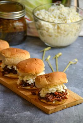 several balsamic & honey pulled pork sliders served on a narrow wooden cutting board with coleslaw and extra barbecue sauce in the background