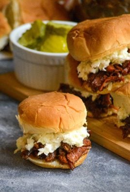 pulled pork sliders shown on a gray background with pickles and fresh rolls in the background