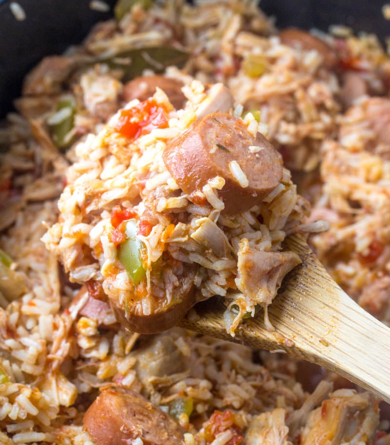 a wooden spoon scooping out the cooked chicken, sausage, and rice