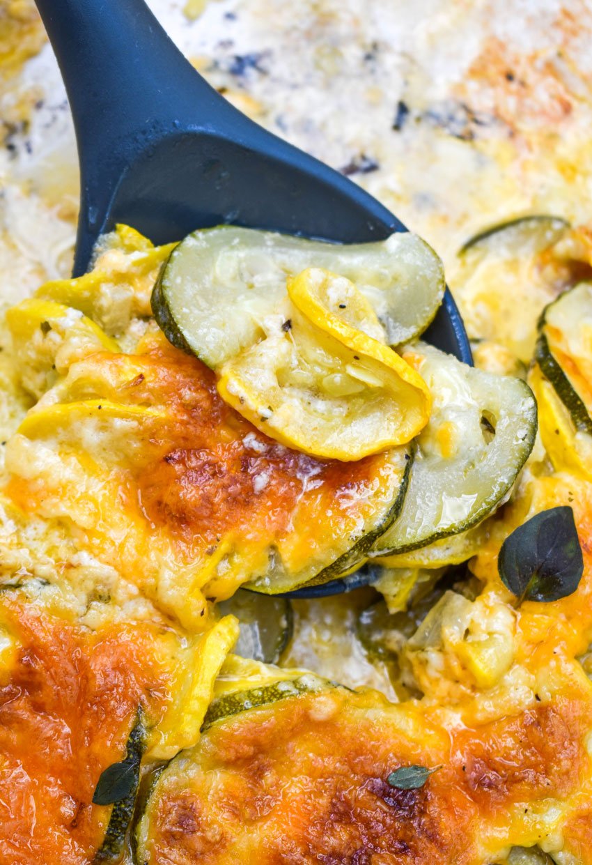 a black serving spoon scooping zucchini gratin with yellow squash out of a skillet