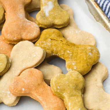 a batch of homemade dog treats shaped like bones and piled together on a parchment paper covered baking pan