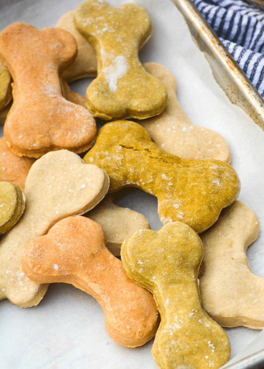 a batch of homemade dog treats shaped like bones and piled together on a parchment paper covered baking pan